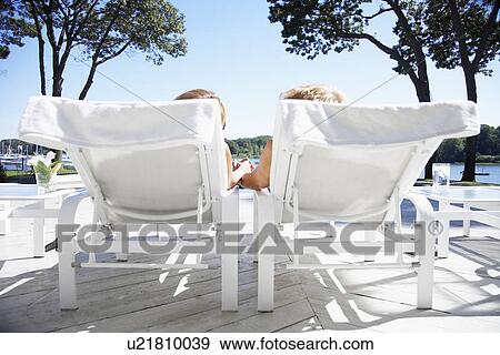 Stock Photo - Couple holding hands and lying on lounge chairs. Fotosearch