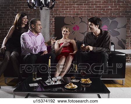 Stock Image - Four friends with drinks at party. Fotosearch