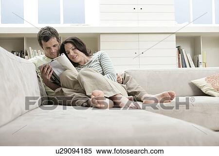 Mid adult couple reading magazine on sofa View Large Photo Image Stock Photography - Mid adult couple reading magazine on sofa. Fotosearch