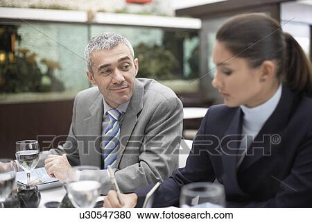Stock Image - Businessman looking at woman making notes. Fotosearch