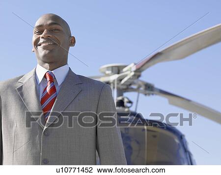 Stock Image - Businessman standing by helicopter (portrait, low angle view). Fotosearch