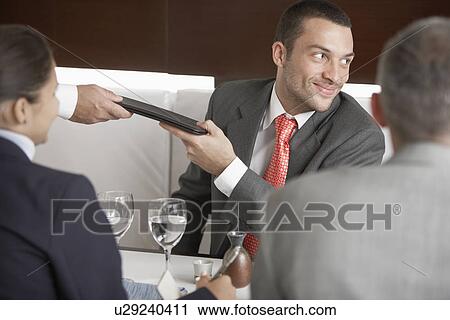 Stock Image - Businessman taking menu at dining table. Fotosearch