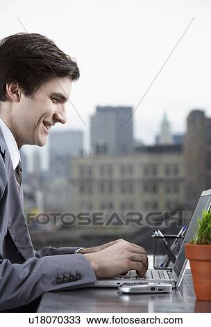 Stock Image - Businessman typing with laptop and smiling. Fotosearch