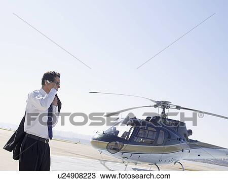 Stock Image - Businessman using cell phone near helicopter. Fotosearch