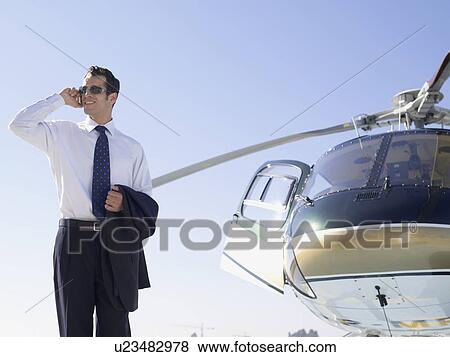 Stock Photo - Businessman using cell phone near helicopter (low angle view). Fotosearch