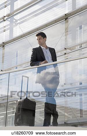 Stock Photo - Businessman with luggage leaning on railing. Fotosearch