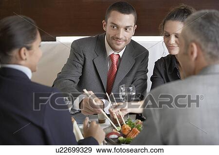 Stock Photo - Four businesspeople having lunch in sushi restaurant. Fotosearch