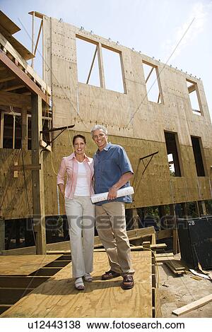 Caucasian mid-adult male holding blue prints with arm around mid-adult female in building construction site. View Large Photo Image Stock Photo - Caucasian mid-adult male holding blue prints with arm around mid-adult female in building construction site.. Fotosearch