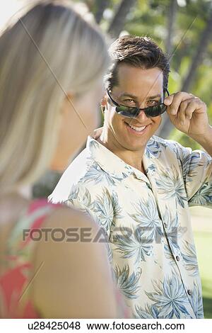 Stock Photo - Caucasian mid adult man tilting sunglasses at woman.. Fotosearch