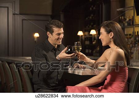 Picture - Couple at bar toasting wine glasses and smiling. Fotosearch