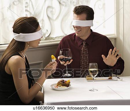 Stock Image - Couple dining in a restaurant with blindfolds over eyes. Fotosearch