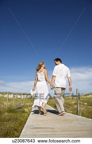 Stock Image - Couple holding hands walking down beach access path. Fotosearch