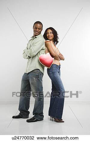 Stock Image - Couple standing back to back holding valentine heart. Fotosearch