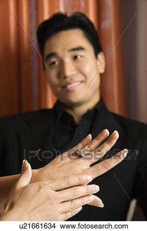 Picture - Female admiring engagement ring with male in background. Fotosearch