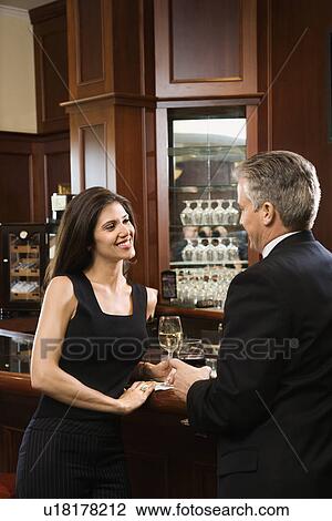 Stock Image - Female and male standing at bar talking. Fotosearch