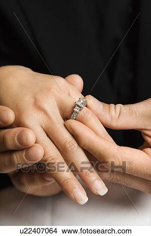 Picture - Male putting engagement ring on female's hand. Fotosearch