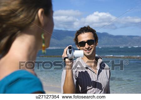 Man on beach pointing video camera at woman View Large Photo Image Picture - Man on beach pointing video camera at woman. Fotosearch