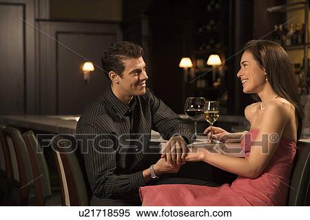 Stock Photography - Mid adult Caucasian couple at bar holding hands and smiling.. Fotosearch