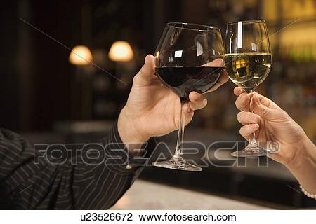 Stock Image - Mid adult Caucasian male and female hands toasting wine glasses.. Fotosearch