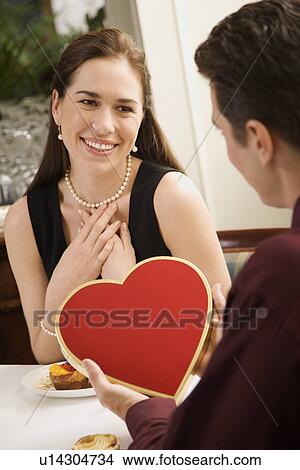 Picture - Mid adult Caucasian man giving a heart shaped box of chocolates to woman at restaurant.. Fotosearch
