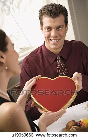Mid adult Caucasian man giving a heart shaped box of chocolates to surprised woman at restaurant. View Large Photo Image Stock Image - Mid adult Caucasian man giving a heart shaped box of chocolates to surprised woman at restaurant.. Fotosearch