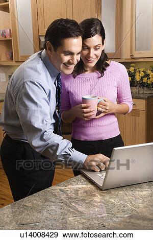 MId-adult couple looking at laptop computer while drinking coffee in kitchen. View Large Photo Image Stock Photo - MId-adult couple looking at laptop computer while drinking coffee in kitchen.. Fotosearch