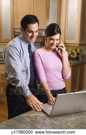 MId-adult female talking on phone and mid-adult male both looking at laptop computer in kitchen. View Large Photo Image Stock Image - MId-adult female talking on phone and mid-adult male both looking at laptop computer in kitchen.. Fotosearch