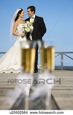 Picture - Pair of flute glasses of champagne with Caucasian bride and groom in background.. Fotosearch