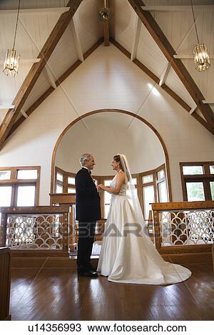 Stock Image - Portrait of bride and groom holding hands at the alter of a church. Fotosearch