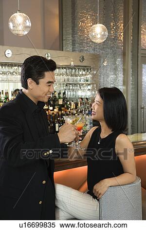 Stock Photography - Prime adult Asian male and female at bar with cocktails.. Fotosearch