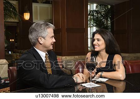 Stock Photo - Prime adult Hispanic female and Caucasian prime adult male sitting at bar talking.. Fotosearch