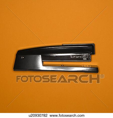 Stock Image - Black stapler on orange background. Fotosearch