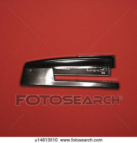 Stock Image - Black stapler on red background.. Fotosearch