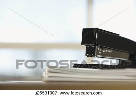 Stock Photo - Black stapler on stack of paper with window in background.. Fotosearch