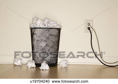 Stock Image - Full wire mesh trash can with crumpled paper next to electrical outlet and plugs.. Fotosearch