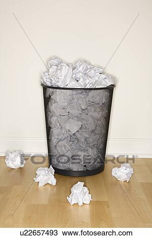 Stock Image - Wire mesh trash can filled and surrounded by crumpled paper.. Fotosearch