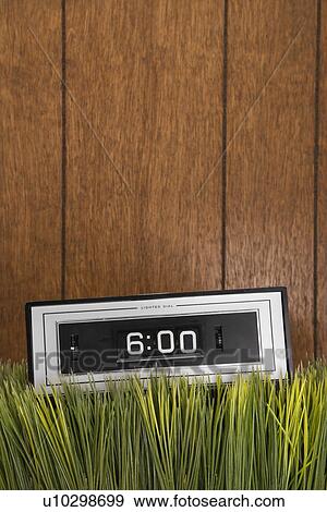 Stock Photo - Studio shot of retro alarm clock placed in grass with wood paneling in background. Fotosearch