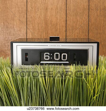 Stock Photograph - Studio shot of retro alarm clock placed in grass with wood paneling in background.. Fotosearch