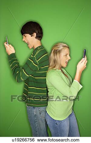 Stock Photograph - Boy and girl on cellphones standing with backs to each other. Fotosearch