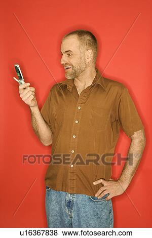 Caucasian man smiling and looking at cellphone standing against orange background. View Large Photo Image Stock Photo - Caucasian man smiling and looking at cellphone standing against orange background.. Fotosearch