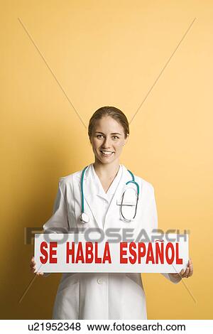 Stock Photo - Female doctor holding up se habla espanol sign. Fotosearch