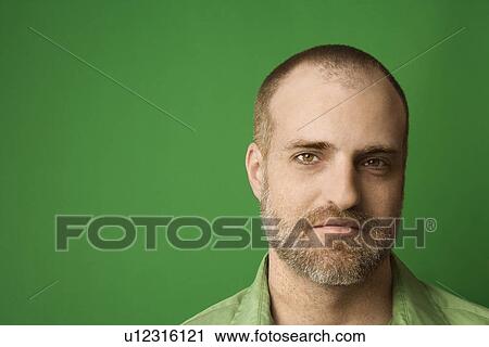 Stock Image - Head shot of Caucasian man with beard and receding hairline against green background.. Fotosearch