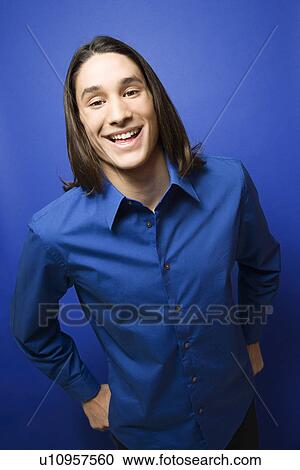 Stock Image - Portrait of Asian-American teen boy smiling at camera against blue background.. Fotosearch