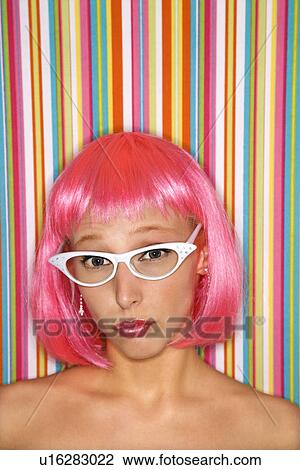 Stock Image - Portrait of attractive young adult woman wearing pink wig against striped background looking at viewer. Fotosearch