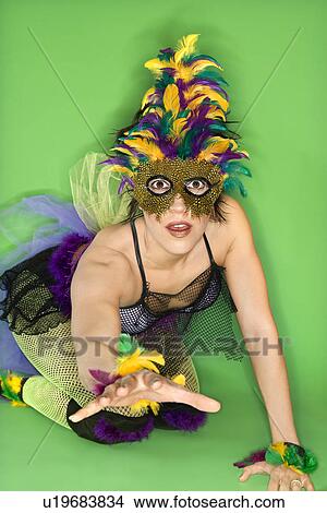 Picture - Portrait of Hispanic woman in Mardi Gras type costume and mask kneeling on floor with hand reaching out against green background.. Fotosearch