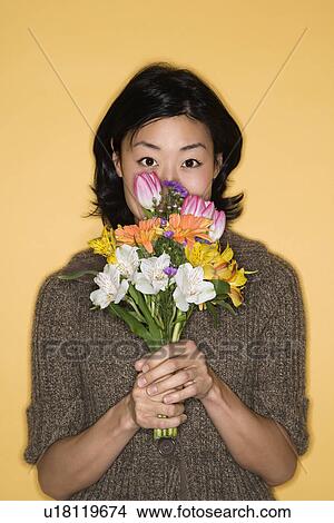 Picture - Pretty mid adult Asian woman holding bouquet of flowers up to face.. Fotosearch
