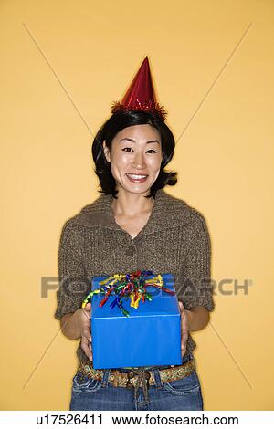Pretty mid adult Asian woman wearing party hat holding present. View Large Photo Image Stock Image - Pretty mid adult Asian woman wearing party hat holding present.. Fotosearch