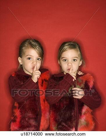 Stock Image - Twins with fingers up to lips. Fotosearch