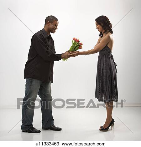 Stock Photo - African American mid adult man giving woman bouquet of flowers.. Fotosearch