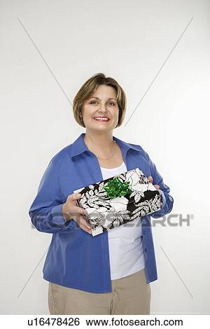 Stock Photograph - Caucasian middle aged woman holding present and smiling at viewer.. Fotosearch